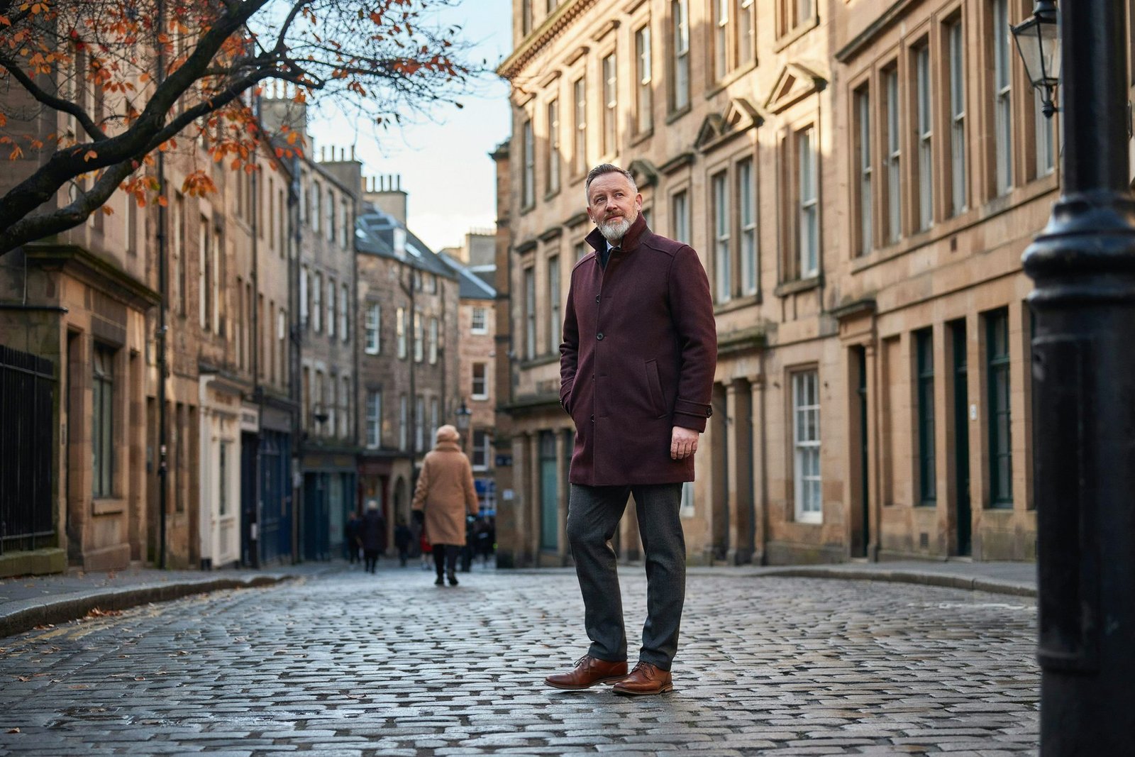 Older adult walking along the Royal Mile in Edinburgh on a crisp autumn morning, planning this winter's flu and Covid vaccines
