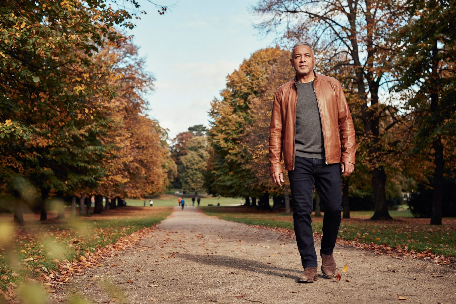 Adult walking under turning trees in the Meadows, Edinburgh, on a bright autumn afternoon during flu vaccination season